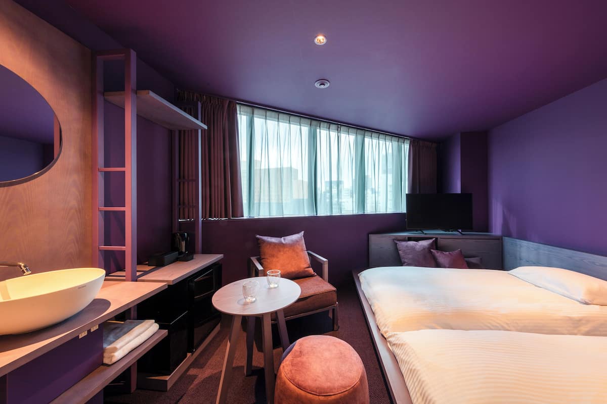 A modern hotel room with a large bed, a desk with a sink, a chair, and a television.