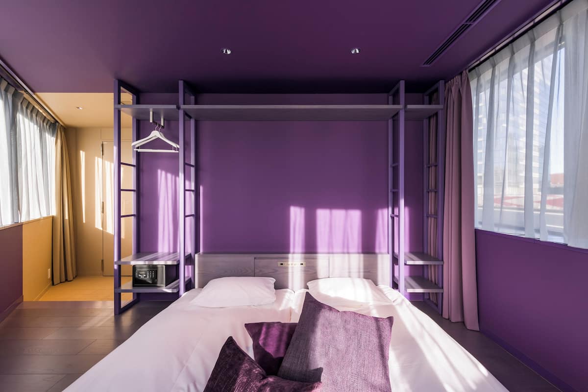 A modern room with a purple wall, a bed with white bedding, and a hanging rack.