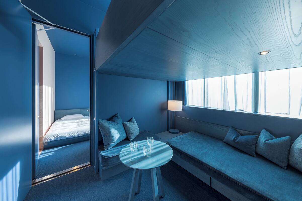 A modern hotel room with a large bed, a seating area with a table, and a window providing natural light.