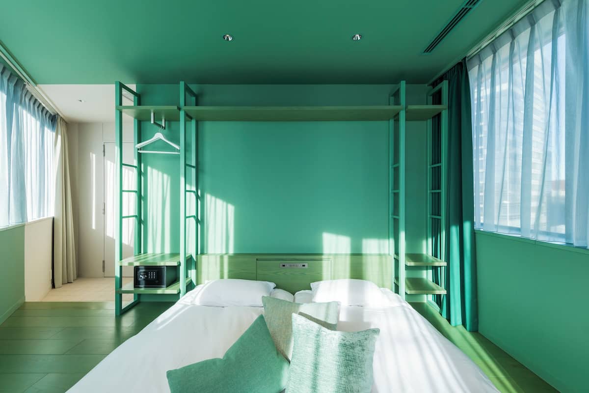 A room with a bunk bed, a bedside table, a hanging coat rack, and a window with curtains.