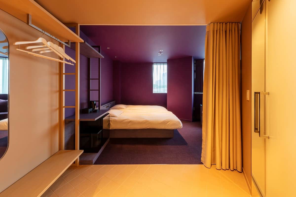 A bedroom with a bed, a wardrobe, a desk, and a mirror.