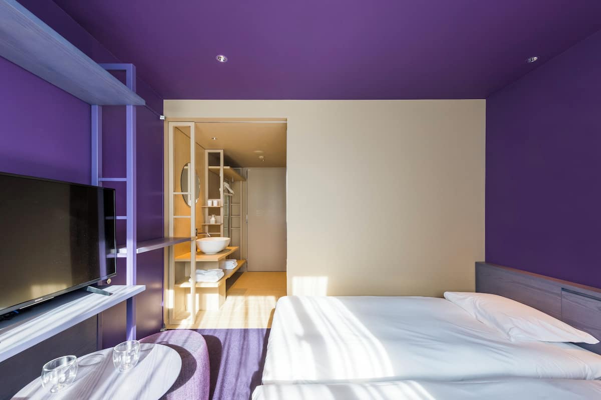 A modern hotel room with a bed, a TV, and a bathroom visible through an open door.