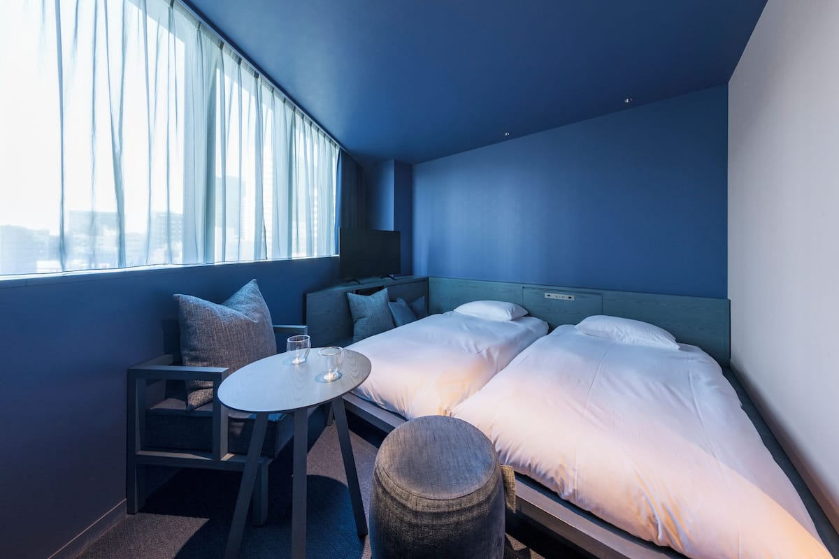 A hotel room with two beds, a small table, and a chair.