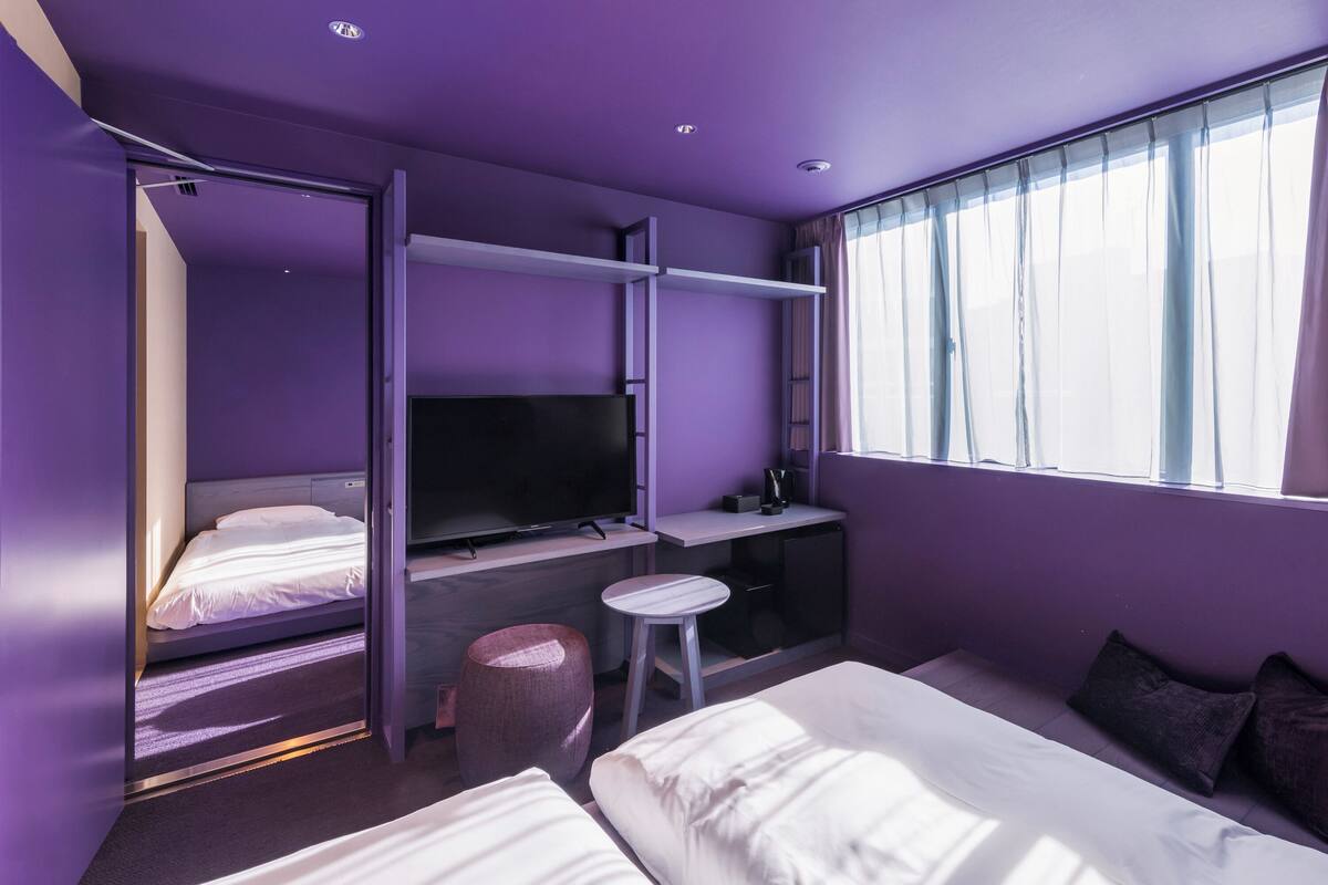 A modern hotel room with a bed, a desk, a TV, and a window with curtains.