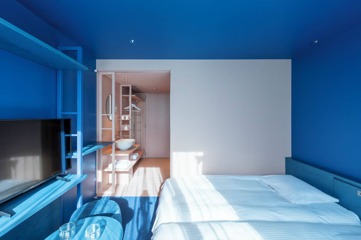 A modern hotel room with a large bed, a TV, and a walk-in closet.