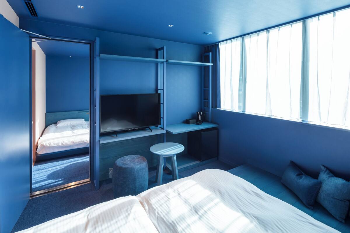 A compact hotel room with a bunk bed, a desk, a television, and a window with curtains.