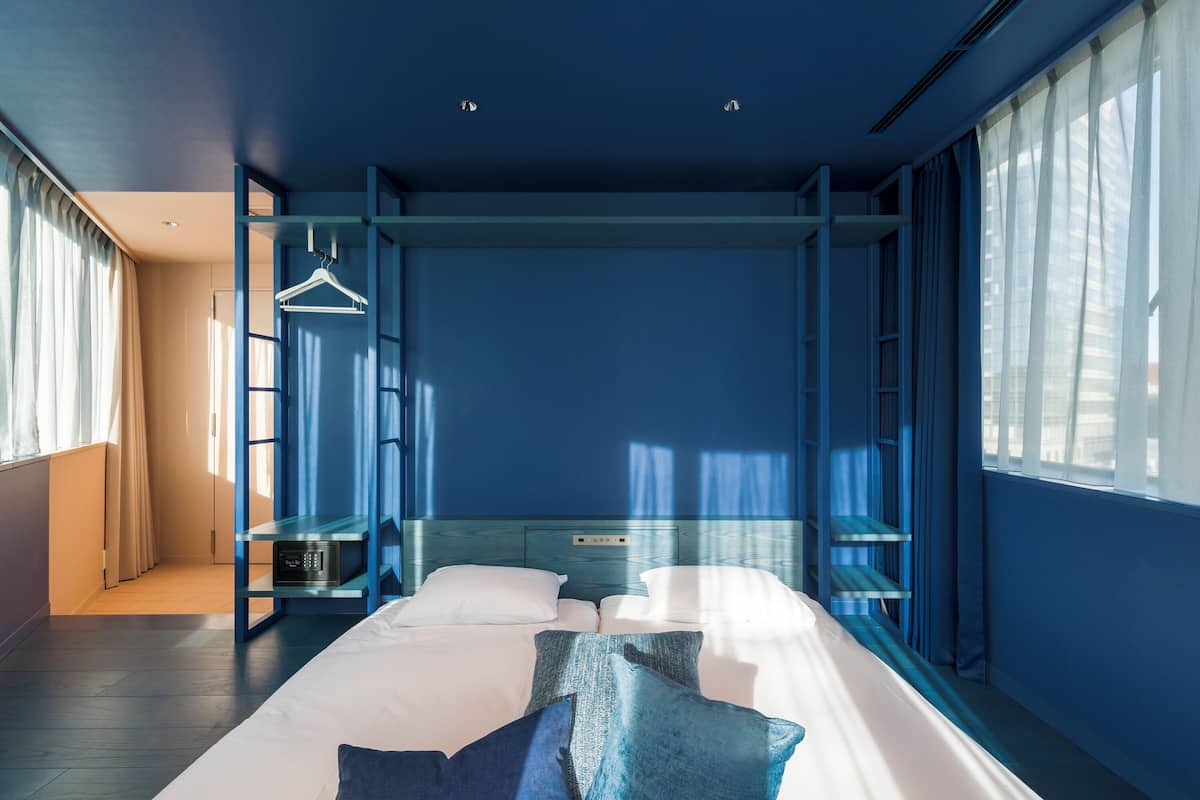 A modern hotel room with a large bed, a wardrobe, and a seating area with a table and chairs.