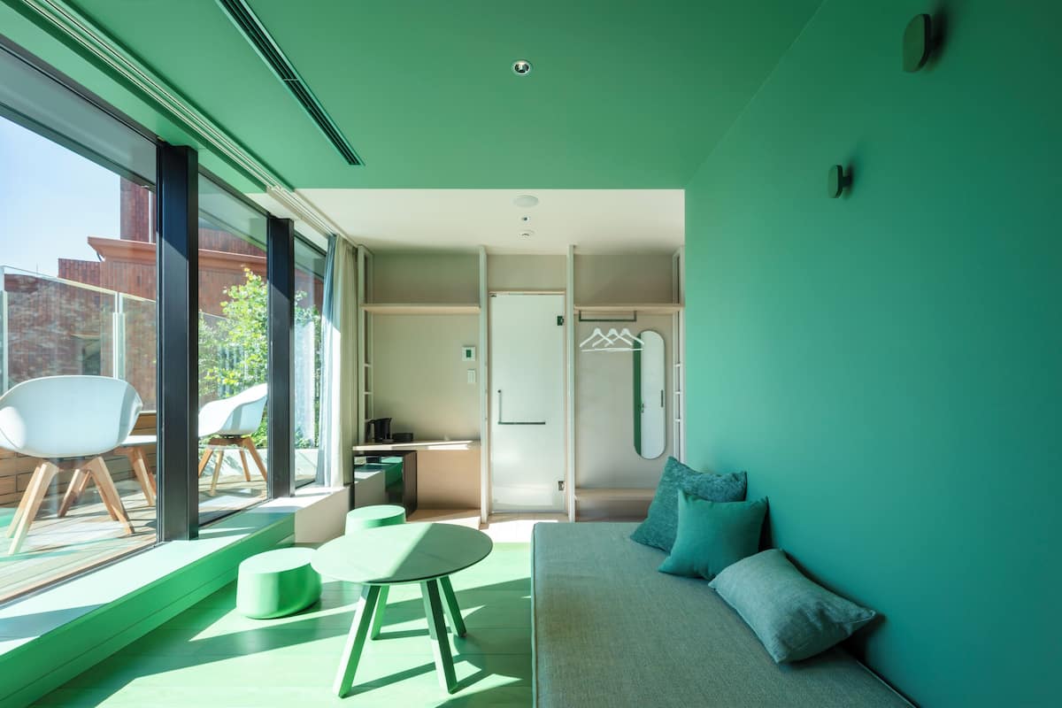 A modern interior with a green wall, a sofa with cushions, a round table, and a chair.