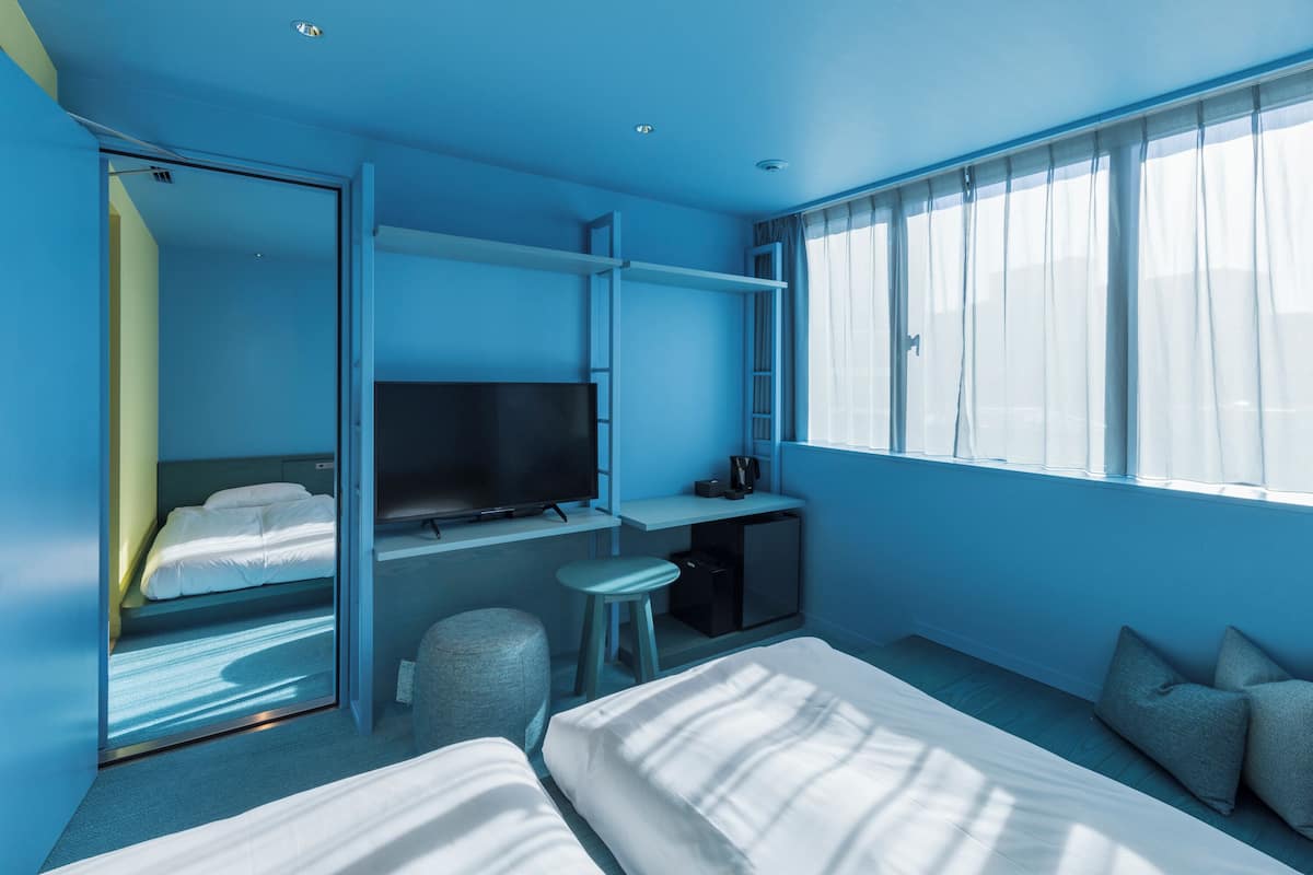 A modern hotel room with a bed, a desk, a TV, and a large window.