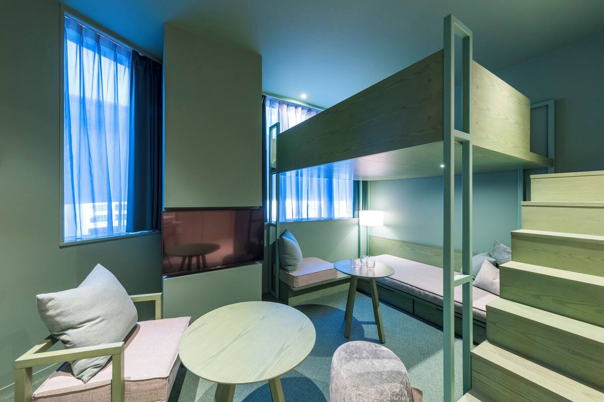 A compact room with a bunk bed, a small table, and a sofa.