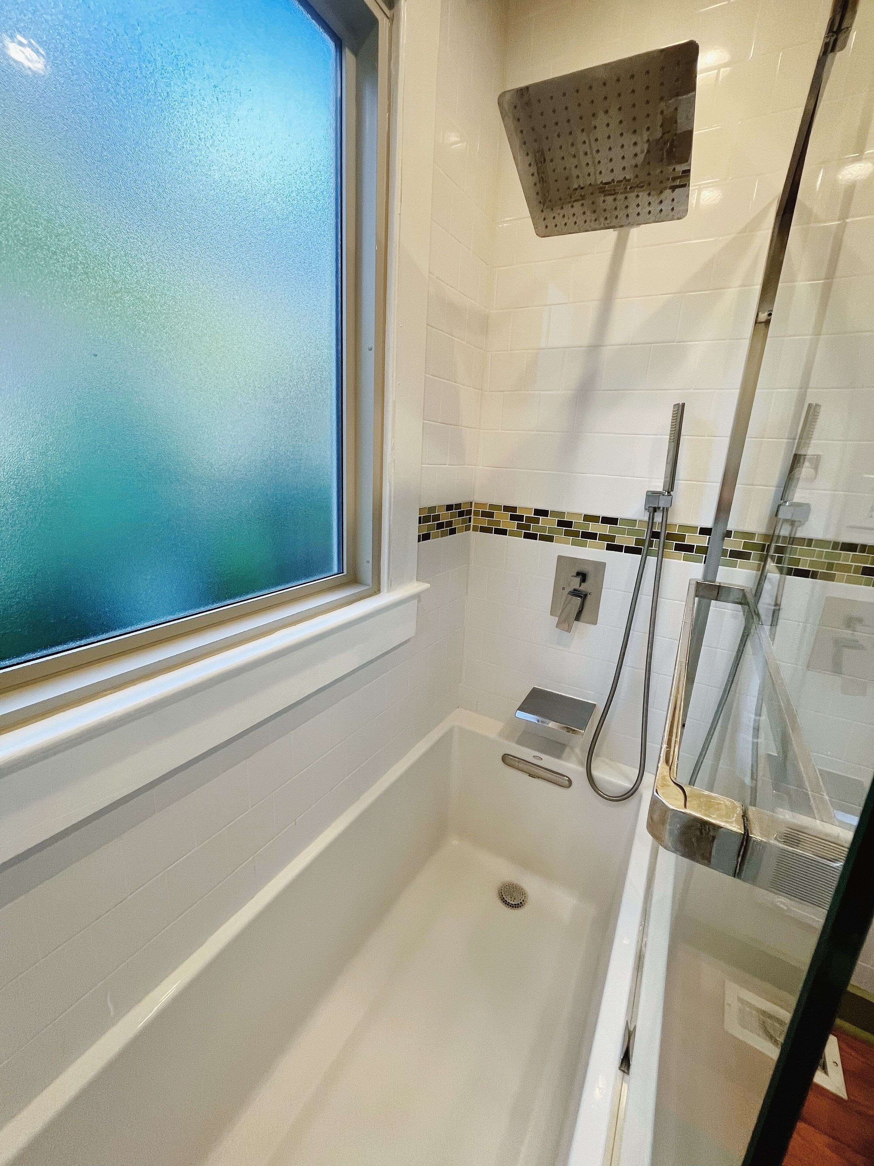 Une petite salle de bain moderne avec une douche à parois de verre, une fenêtre et un mur recouvert de carreaux.