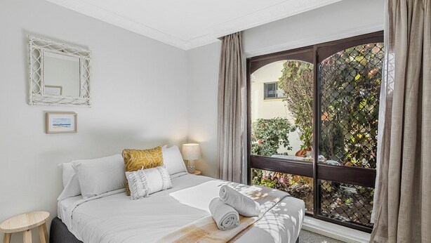 Une chambre d’hôtel avec un lit, une table de chevet, une lampe, un tableau encadré et une fenêtre avec des rideaux.