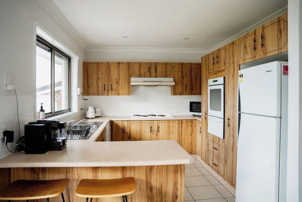 Una cocina moderna con armarios de madera, encimera blanca, horno empotrado, microondas y refrigerador.