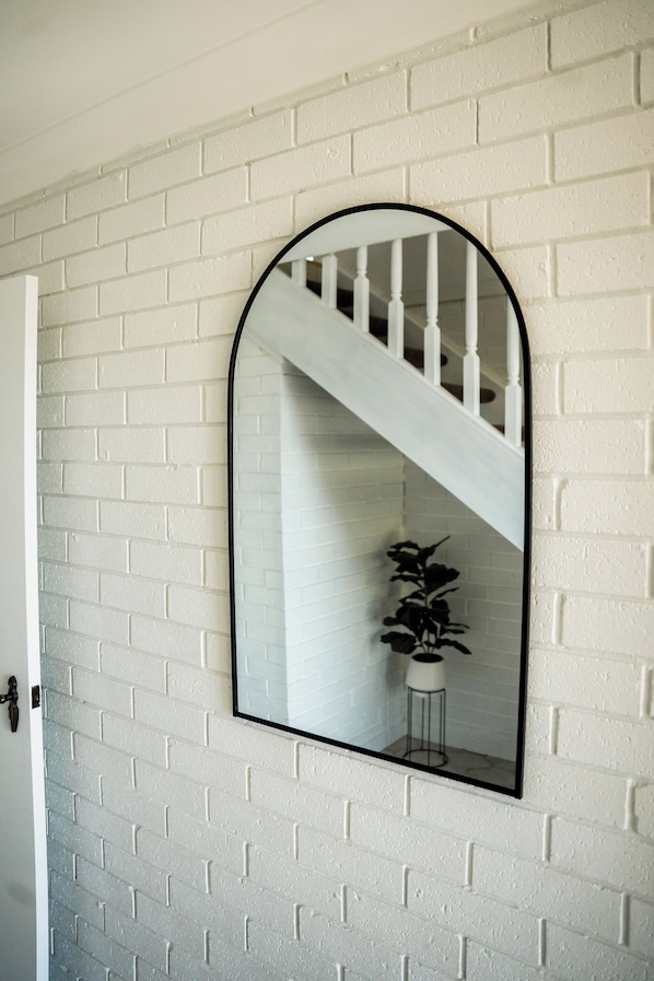 A white brick wall with a large mirror reflecting a staircase and a plant. - Family getaway with ocean views (Gerroa)