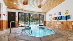 An indoor swimming pool with stone flooring, wooden walls, and a view of the outdoors.