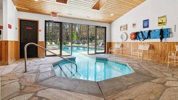 An indoor swimming pool with stone flooring, wooden walls, and a view of the outdoors.