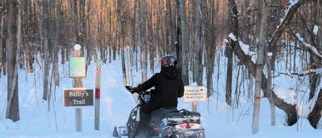 A snowmobile on a trail with signs indicating directions to Bailey's Trail and Pleasantview State Trails.