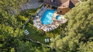 A large, circular swimming pool with a stone deck and lounge chairs, surrounded by a well-maintained lawn and trees.