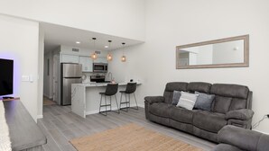 Una sala de estar moderna con un sofá gris, una mesa de centro y una cocina al fondo.