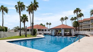 Una piscina con palmeras, un pabellón y una valla blanca.