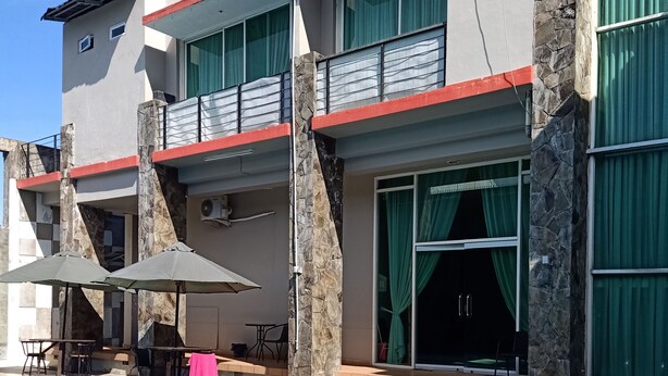 Una piscina con agua azul cristalina, rodeada por un edificio con pilares de piedra, un balcón y una zona de estar cubierta.