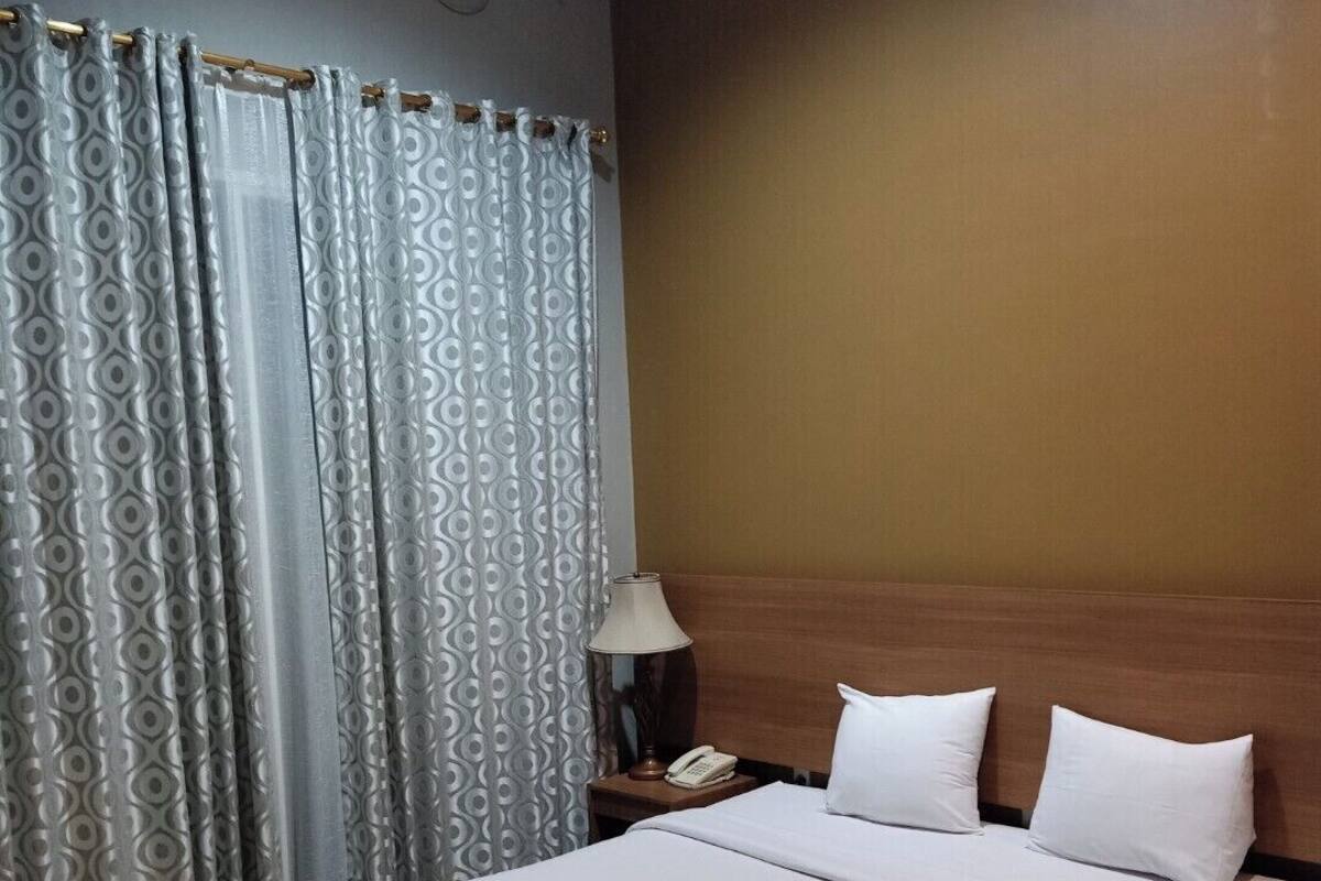 A hotel room with a large bed, a wooden headboard, a bedside table with a lamp, and a telephone.