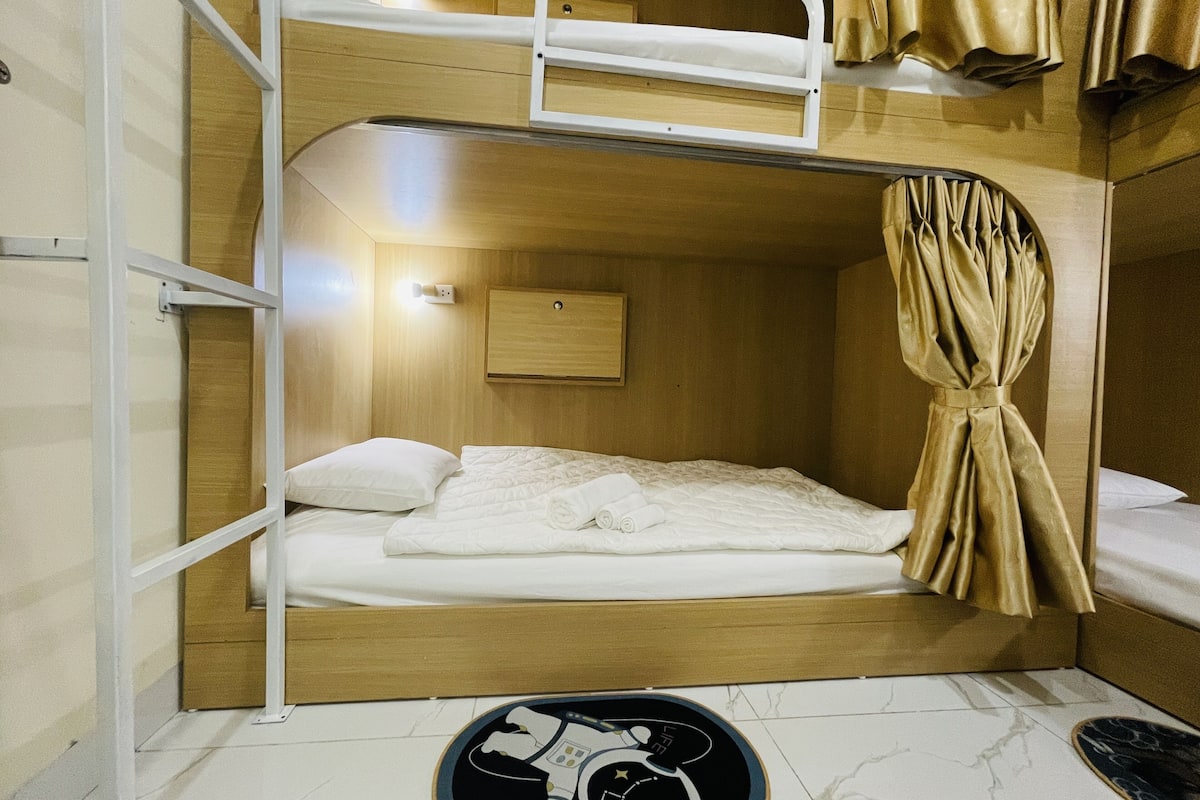 A bunk bed room with a wooden headboard, a small bedside table, and a curtain.