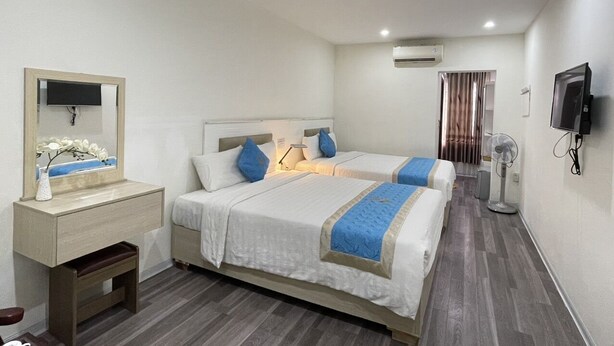 Habitación de hotel con dos camas, una mesita de noche con lámpara, aire acondicionado, televisor y ventilador.