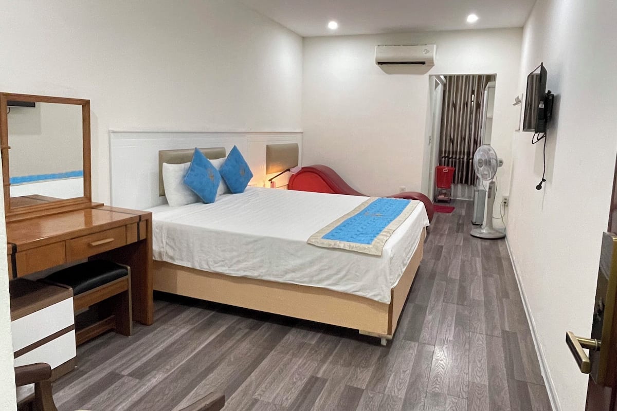 A hotel room with a bed, a desk, a chair, a TV, and an air conditioning unit.