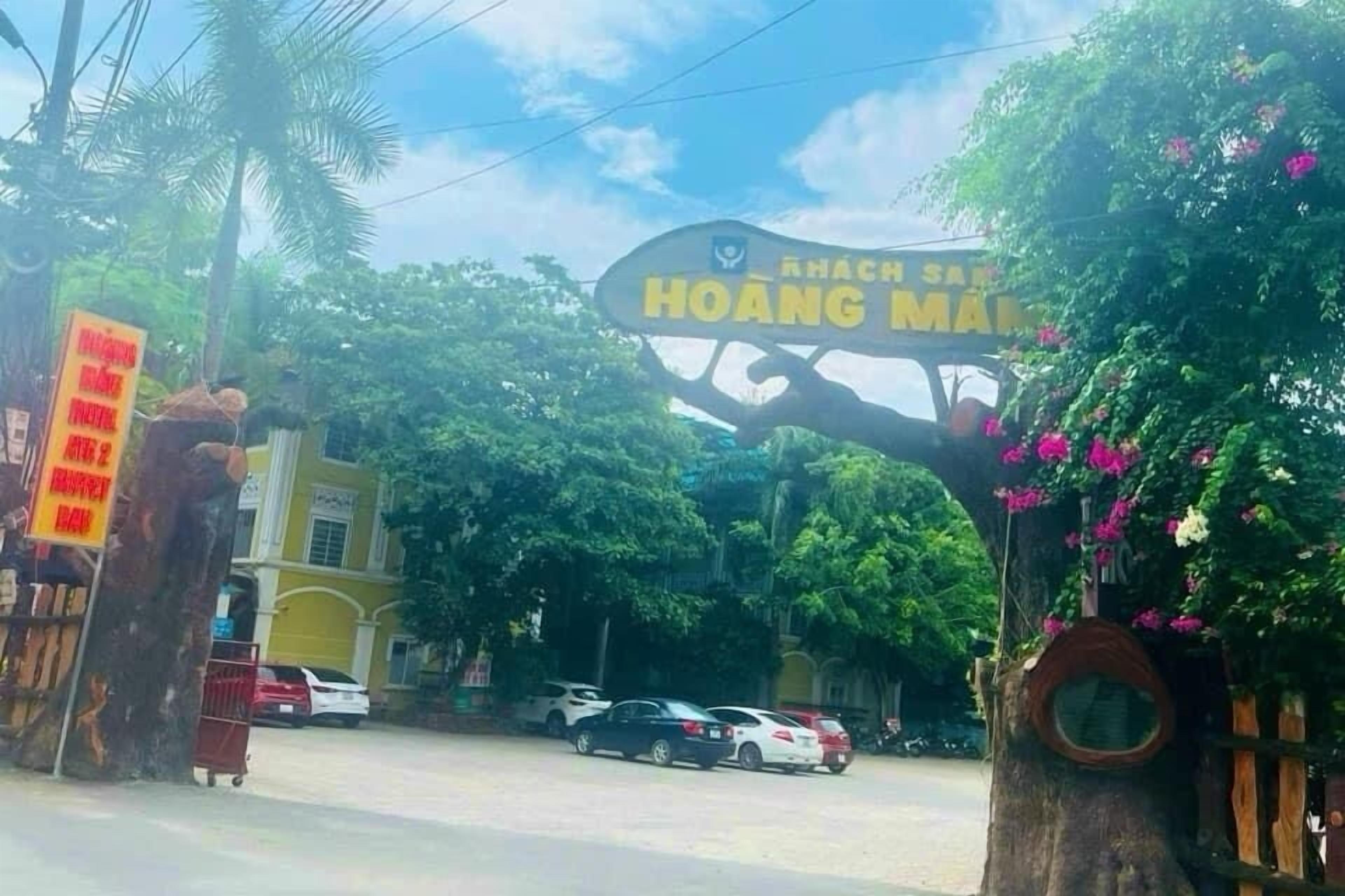 Un senyal amb la inscripció 'HOANG MANG', un arbre amb una finestra circular i un edifici al fons.