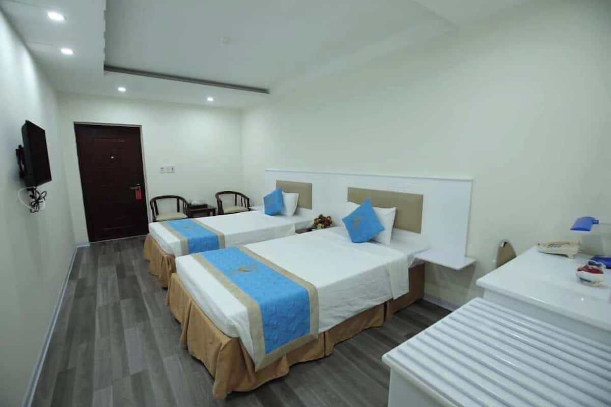 A hotel room with two beds, a desk, a chair, and a TV.