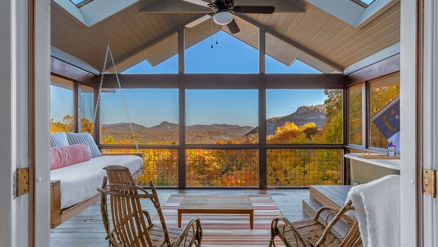 A spacious balcony with a bed, wicker chairs, and a table, overlooking a scenic autumn landscape. - Whiteside Perch - Updated Home w/ Huge Views! Close to Everything!  (Highlands)