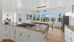 A spacious kitchen with white cabinetry, a granite countertop, and a large island with a stove. There are multiple windows offering views of the outdoors. - Whiteside Perch - Updated Home w/ Huge Views! Close to Everything!  (Highlands)