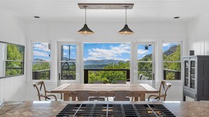 A dining area with a large table, chairs, and a view of mountains through large windows. - Whiteside Perch - Updated Home w/ Huge Views! Close to Everything!  (Highlands)