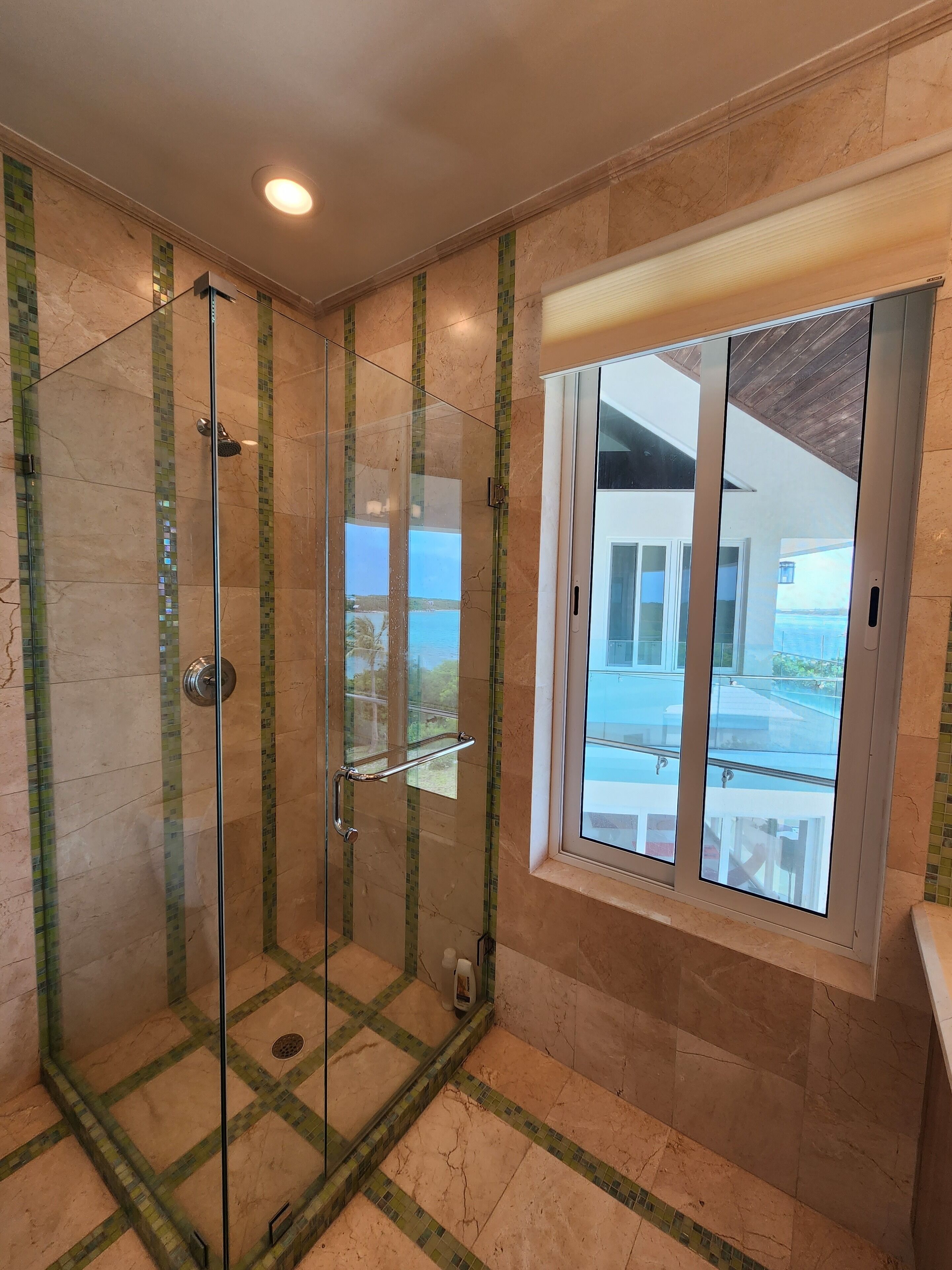 Une douche en verre avec vue sur la mer, une fenêtre donnant sur la mer et un sol carrelé.