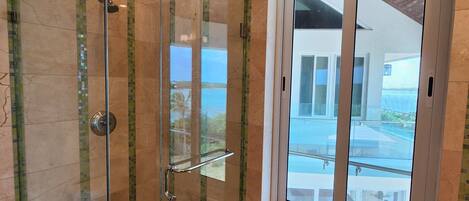 Une douche en verre avec vue sur la mer, une fenêtre donnant sur la mer et un sol carrelé.