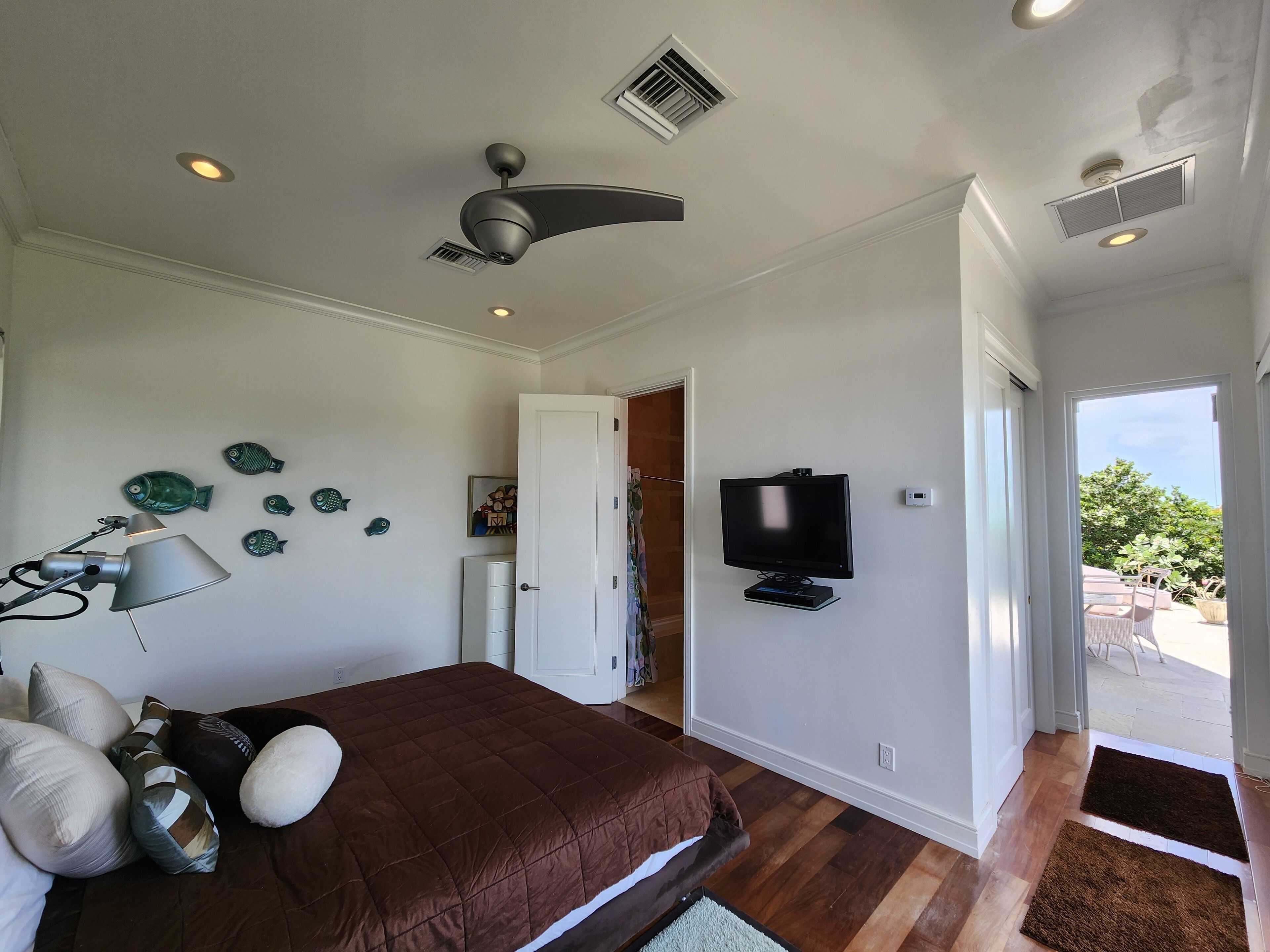 Un dormitorio con cama, ventilador de techo, televisor y puerta que da a un balcón.