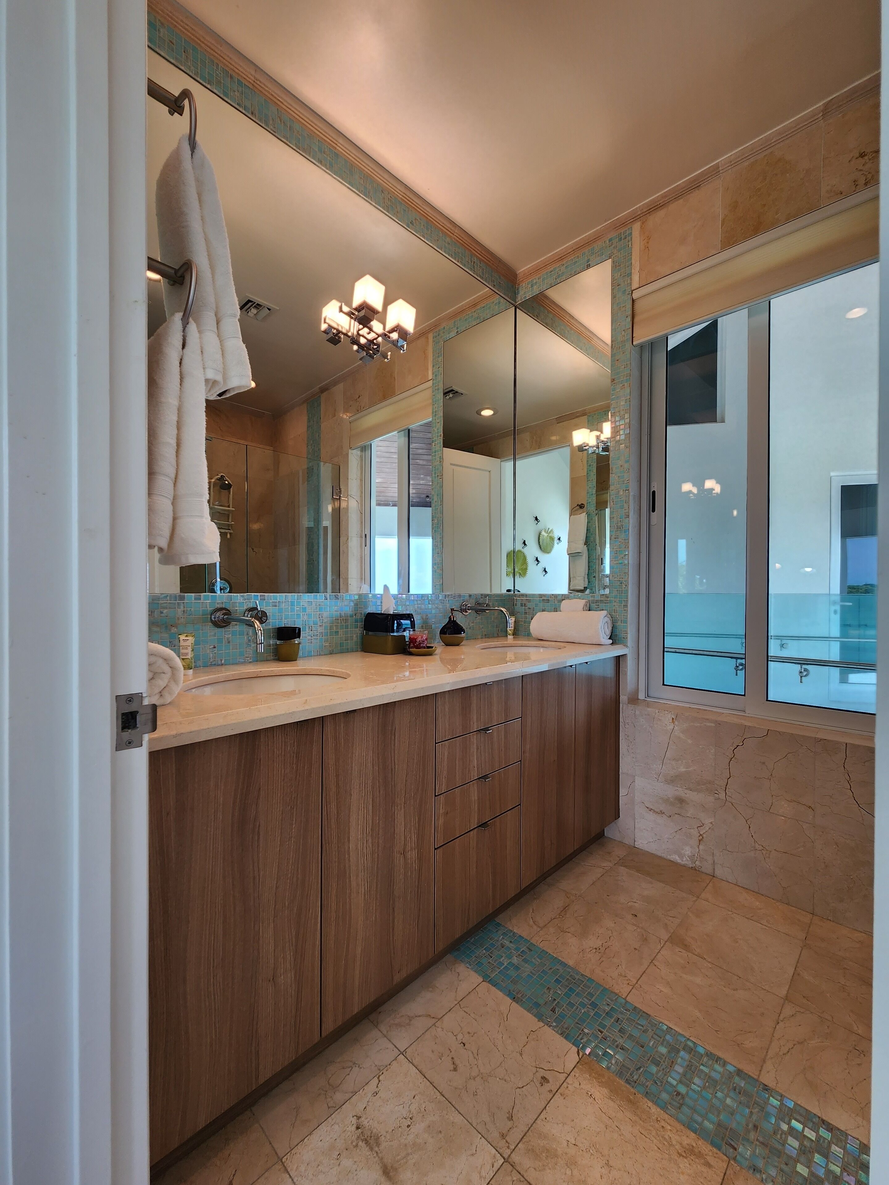 Un baño moderno con un espejo grande, armarios de madera, lavamanos doble y vistas al exterior.