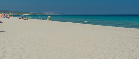 A beach with clear turquoise water, a sandy shore, and a few umbrellas and beach chairs.