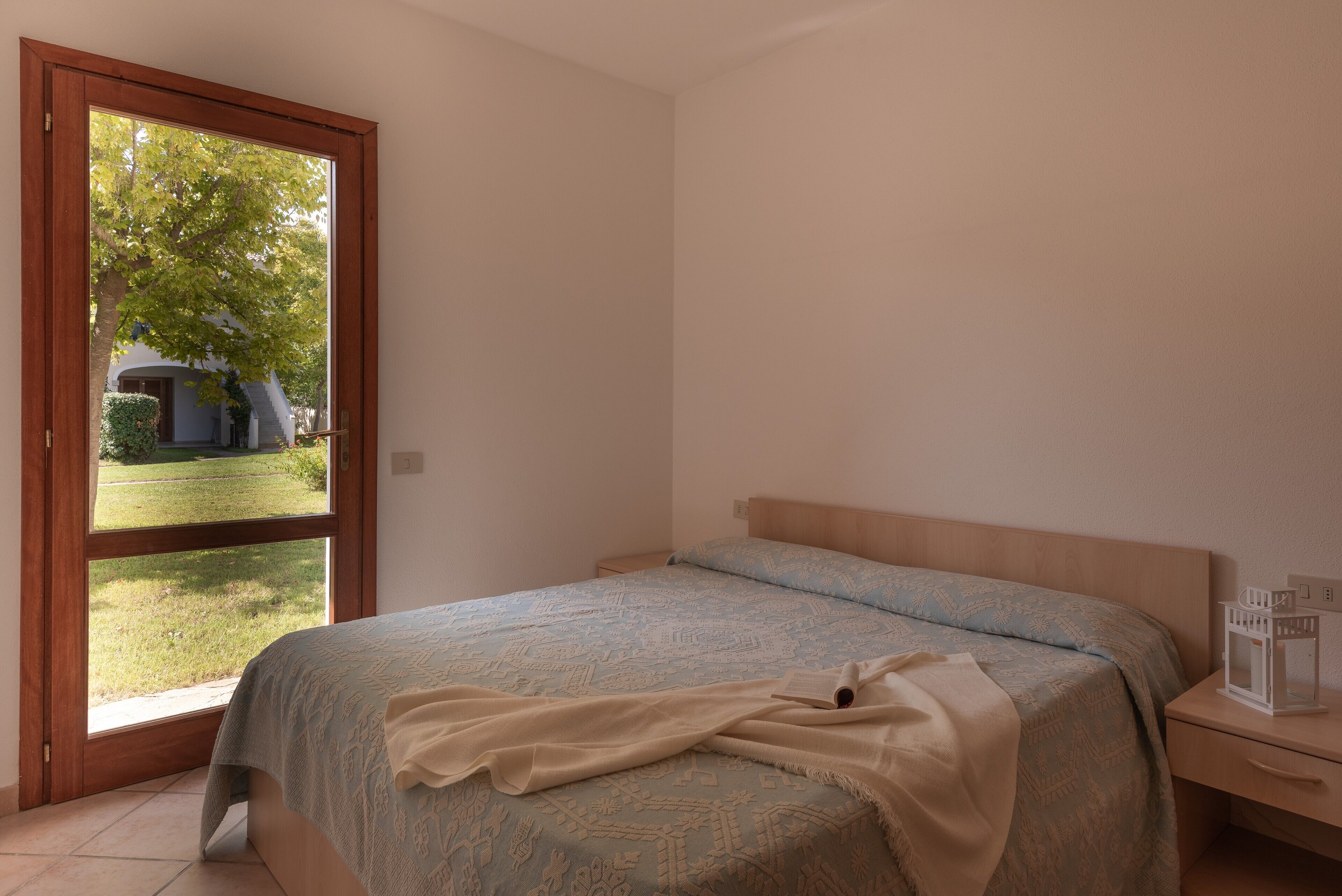 Une chambre à coucher avec un lit, une table de chevet, une fenêtre et une vue sur une maison et une pelouse.