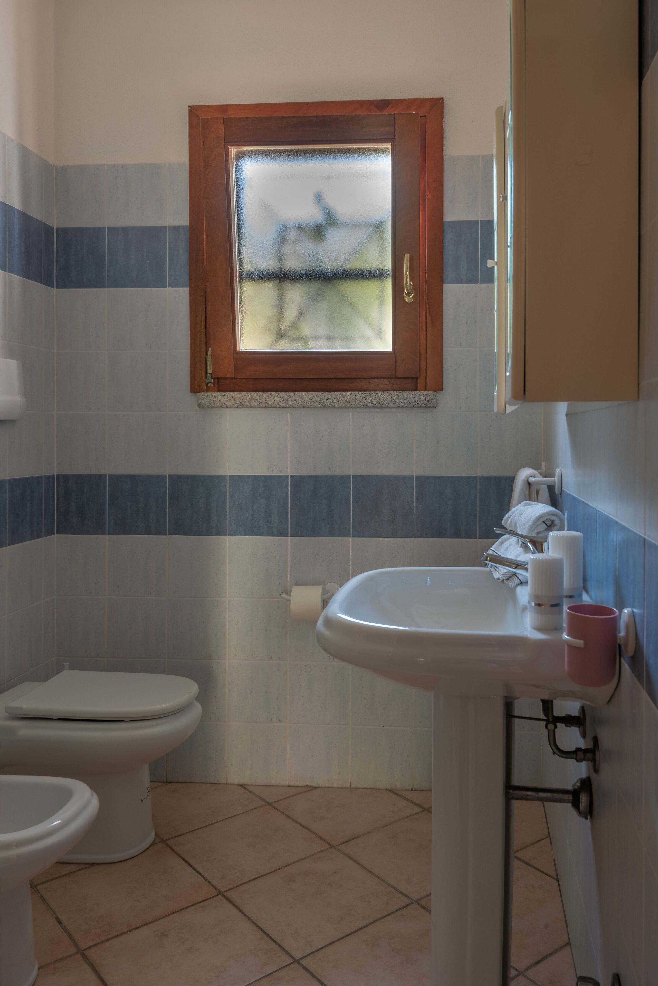 A bathroom with a toilet, sink, and window.