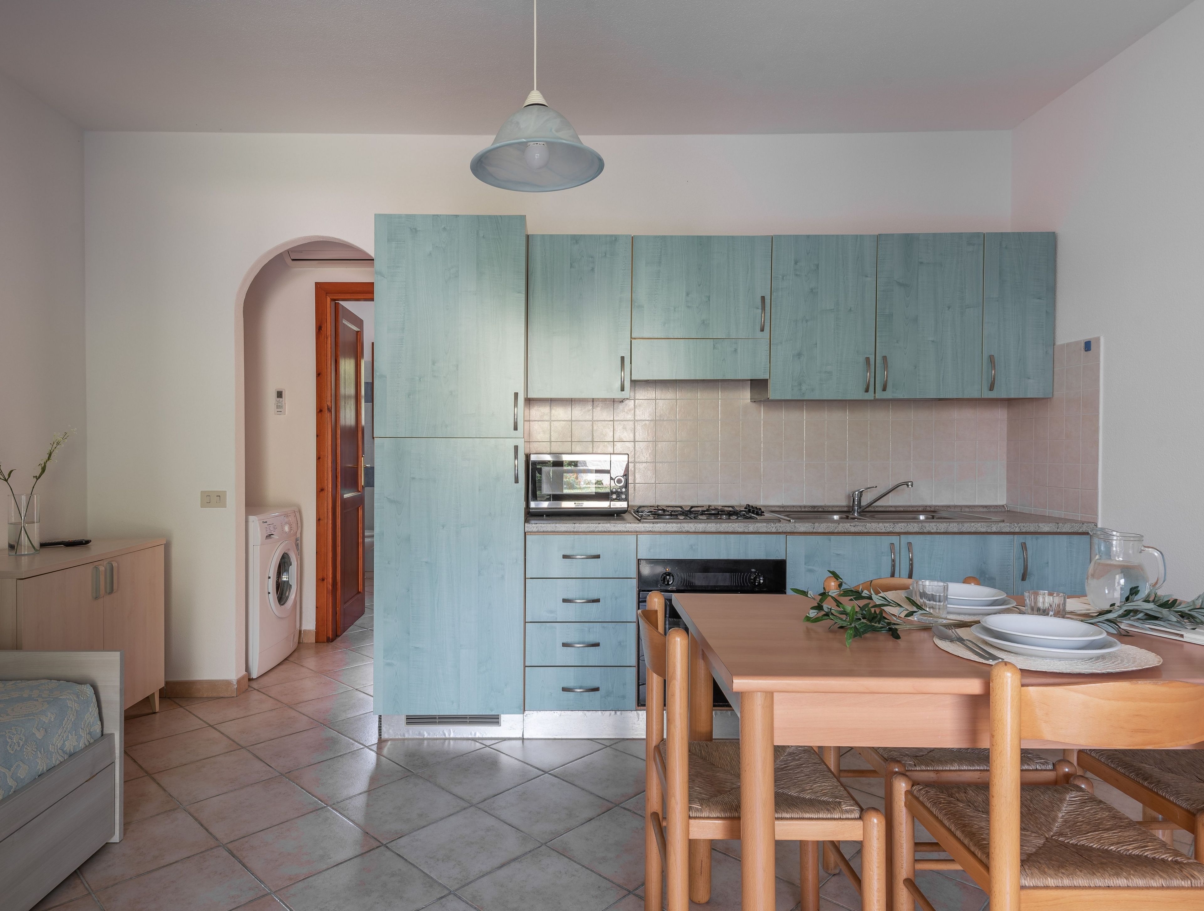 A compact kitchen with teal cabinets, a dining table with chairs, and a washing machine.