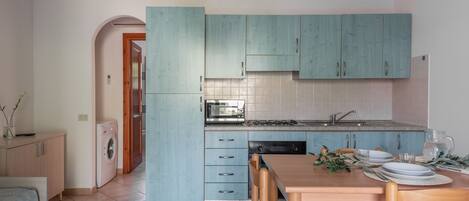 A compact kitchen with teal cabinets, a dining table with chairs, and a washing machine.