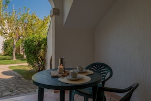 Ein runder Tisch mit zwei Stühlen, einer Kerze und zwei Tassen auf einer Terrasse mit Blick auf einen Garten und ein Gebäude.