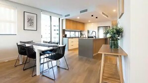 Une cuisine moderne dotée d’un îlot central, de meubles en bois et d’un coin repas avec une table blanche et des chaises noires.
