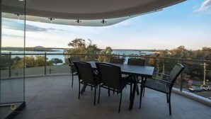 Un balcon avec une table et des chaises, donnant sur une étendue d’eau et un paysage lointain.