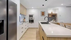 A modern kitchen with a stainless steel refrigerator, built-in oven, microwave, and a large island with a sink. - SEASIDE ESCAPE@ The Cosmopolitan Unit 10406 (Sunshine Coast)