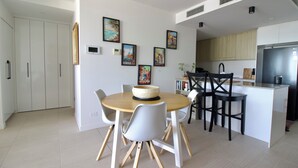 Een moderne keuken met witte kasten, een zwarte koelkast en een eethoek met een ronde houten tafel en witte stoelen.
