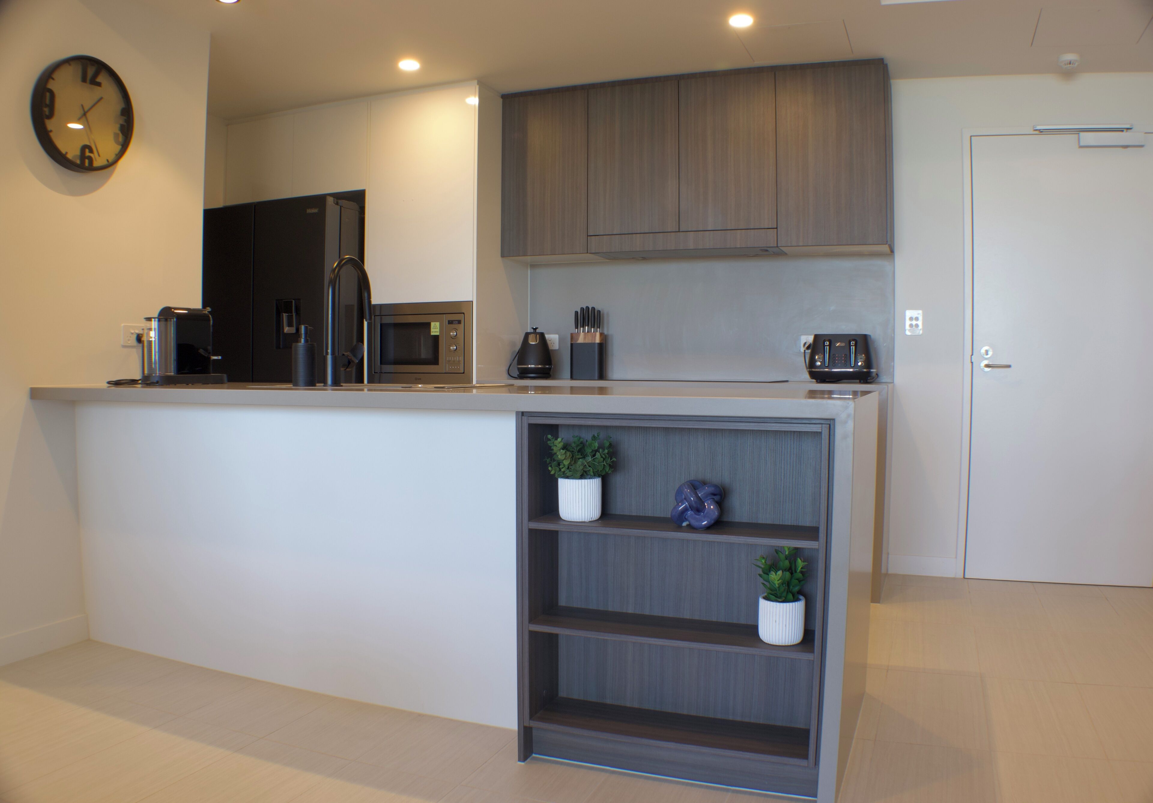 A modern kitchen with a built-in microwave, coffee maker, and a clock on the wall.