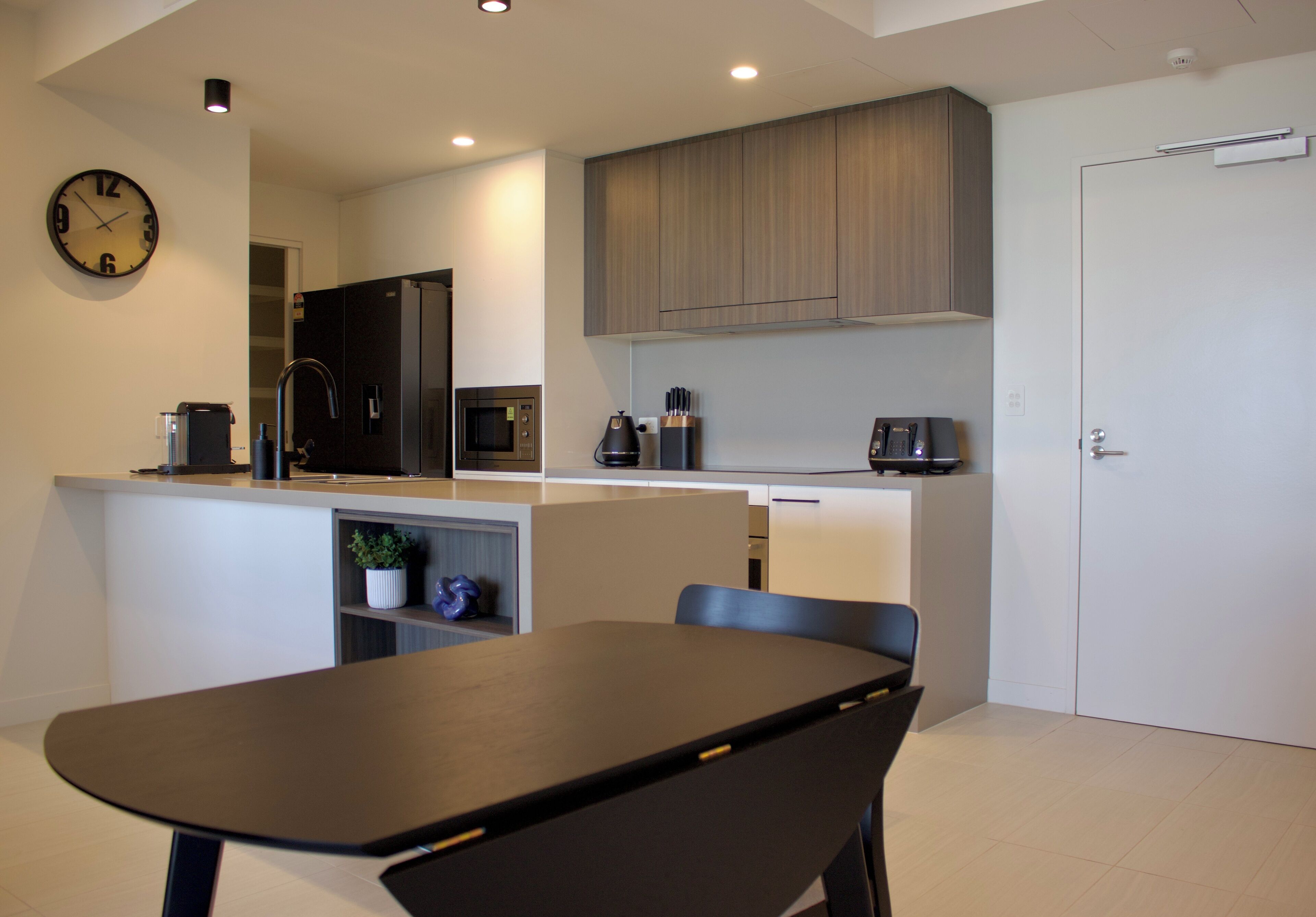 Una cucina moderna con zona pranzo, che include un orologio, un forno a microonde, una macchina per il caffè e un lavandino.